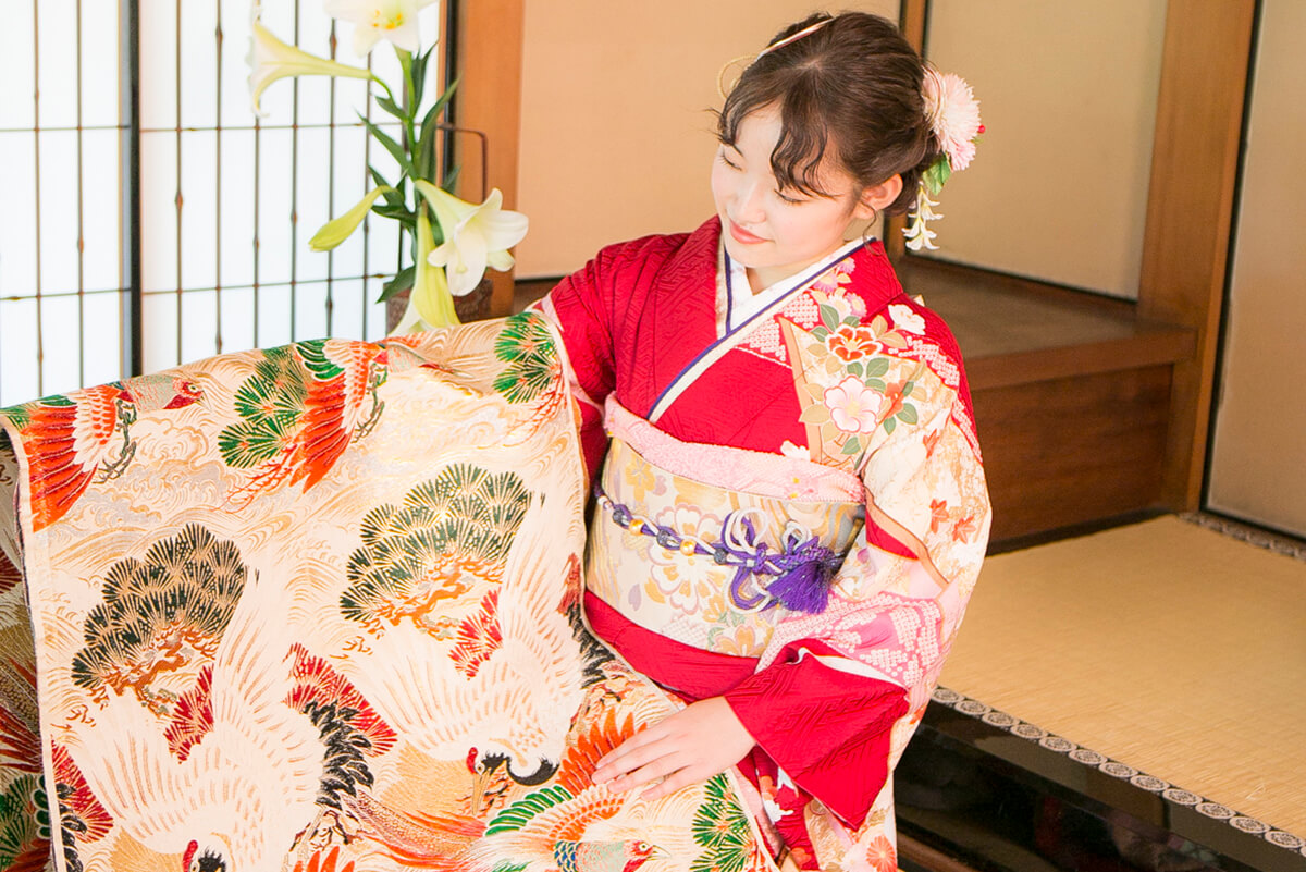 赤い振袖姿の女性が帯を手に持っている